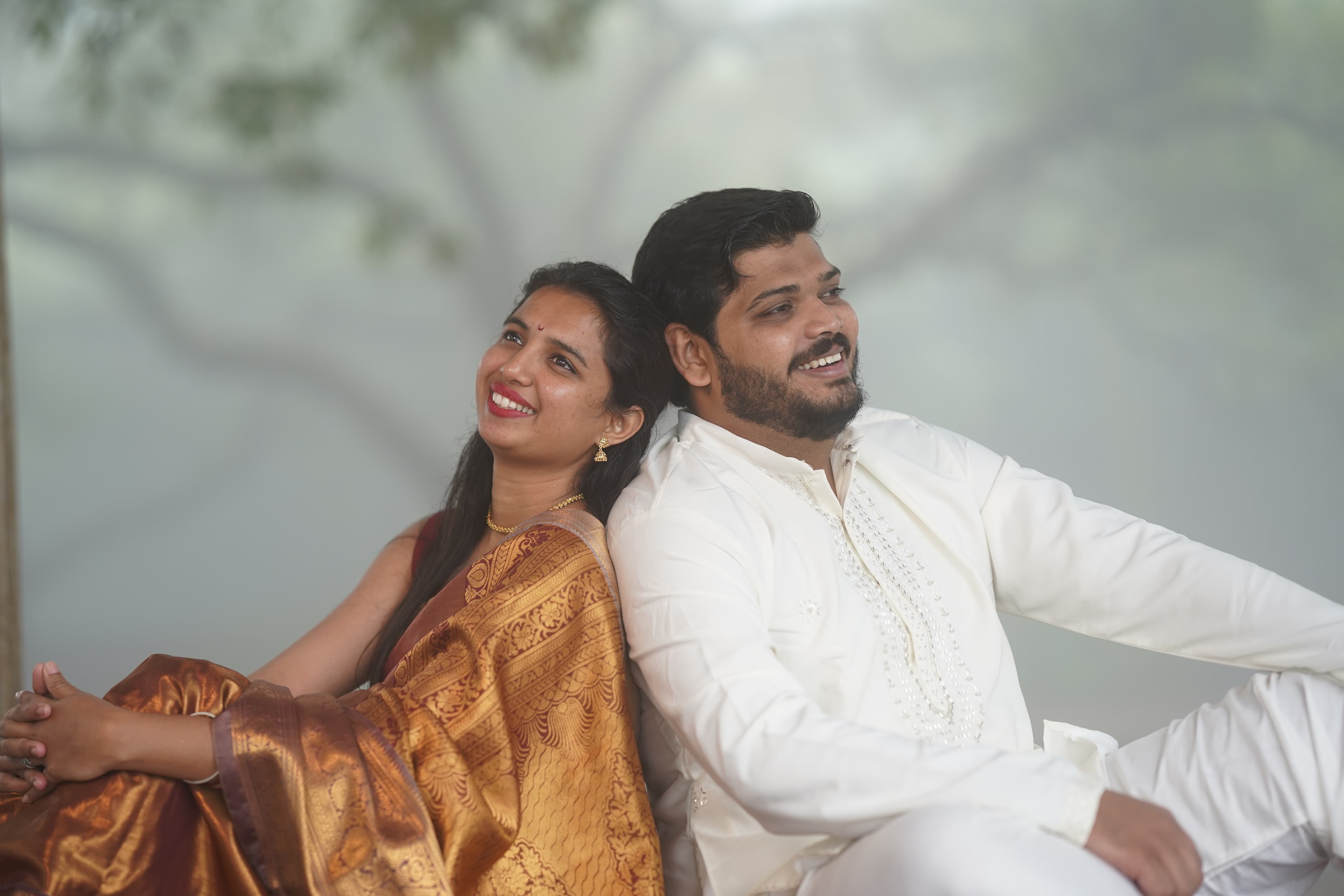 Vineet and Manasi seated back to back, laughing in soft light